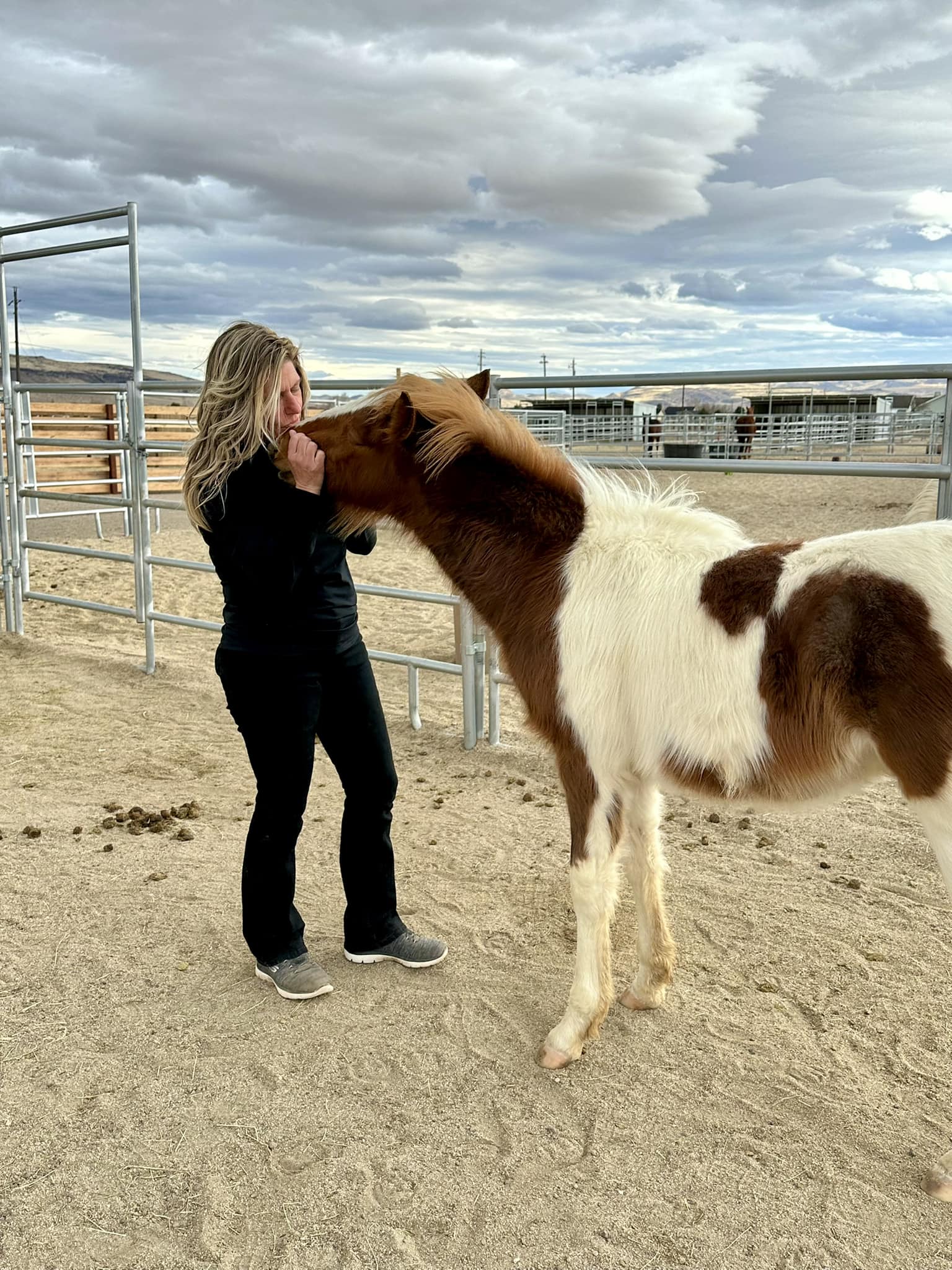 A woman gently pets a horse inside a pen, showcasing a moment of connection between them.